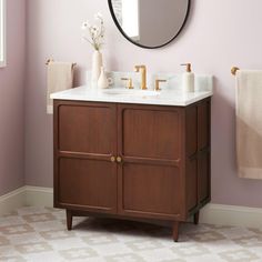 a bathroom with pink walls and a white sink under a round mirror on the wall