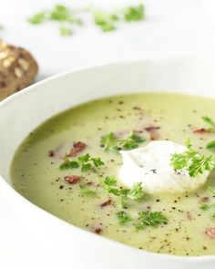 a white bowl filled with broccoli soup next to a piece of bread on top of a table