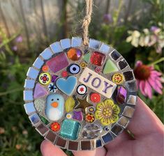 a hand holding up a glass ornament that says joy with colorful buttons and hearts