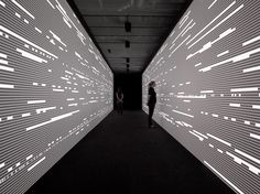 two people are standing in an empty room with white lights on the walls and black carpet