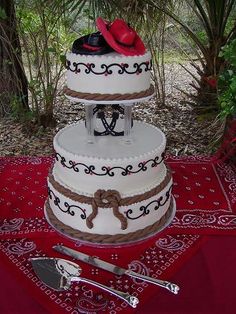 a three tiered cake on a red table cloth with utensils next to it