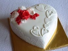 a heart shaped cake with red and white flowers on it sitting on a gold plate