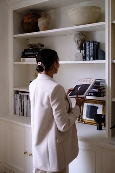 a woman standing in front of a bookshelf holding a magazine and looking at it