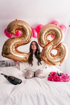 a woman sitting on top of a bed with balloons in the shape of two numbers