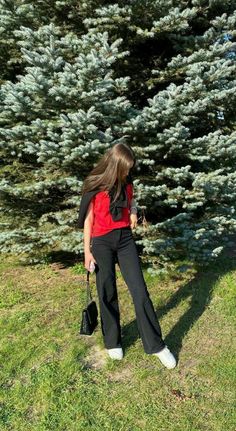 a woman standing in front of a tree with her hand on her hip and looking down at the ground