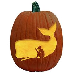 a carved pumpkin with a silhouette of a whale and a man sitting on the ground