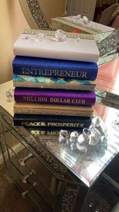 a stack of books sitting on top of a glass table next to a crystal vase