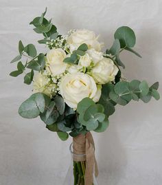 a bouquet of white roses and greenery in a clear glass vase on a table