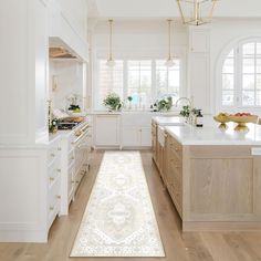 a large kitchen with white cabinets and wooden floors, along with an area rug on the floor