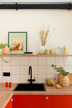 a kitchen with red cabinets and white tiled backsplash, black faucet