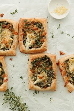 four small square pizzas with different toppings on them sitting on a white surface