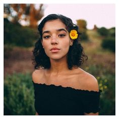 a woman with a yellow flower in her hair is looking at the camera while wearing a black dress