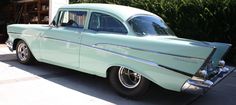 an old green car parked in front of a garage