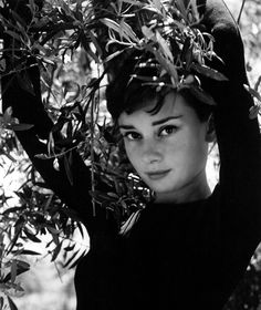 black and white photograph of a woman with her hands on her head, in front of an olive tree