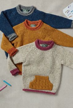 three knitted sweaters are sitting on a table next to crayons and markers