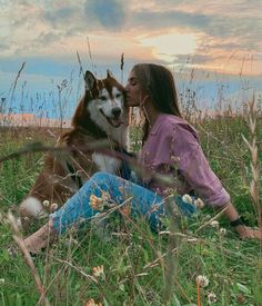 a woman is sitting in the grass with her dog and kissing her face on the ground