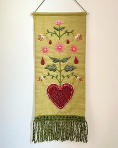 an embroidered wall hanging with flowers and hearts on the front, attached to a white wall