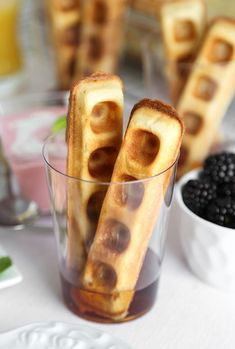 some waffle sticks are in a glass on a table with berries and other food