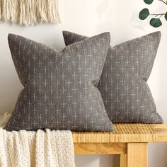 two gray pillows sitting on top of a wooden table next to a plant and wall hanging