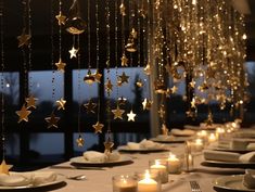 a long table with white plates and silverware on it, lit up by candles