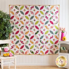 a quilted wall hanging next to a white chair and table with a potted plant