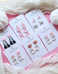 six pairs of earrings are displayed on a pink surface next to white towels and flowers