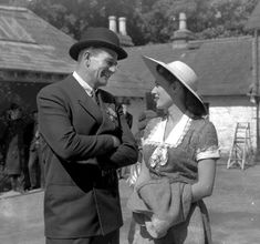 an old black and white photo of two people standing next to each other with hats on