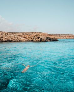 a person swimming in the blue water near some rocks and an island with a rock outcropping