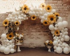 sunflowers and white balloons are arranged in the shape of an arch on a brick wall