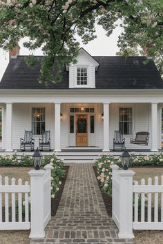 a white house with two rocking chairs on the front porch and a brick walkway leading up to it