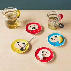 four plates with faces and spoons sitting on a table next to two cups filled with tea