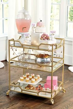 a gold serving cart filled with cupcakes and pastries on top of a hard wood floor