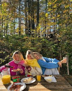 two women sitting at a picnic table with food and orange juices on the side