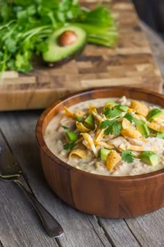 a wooden bowl filled with oatmeal and topped with avocado next to a cutting board