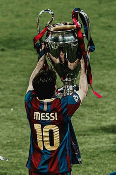 a man holding up a trophy on top of a soccer field with his hands in the air