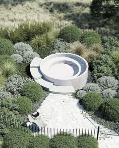 an aerial view of a circular concrete structure surrounded by shrubbery and trees, with a bench in the center