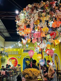 people are sitting at tables in a brightly lit room with lanterns hanging from the ceiling