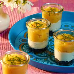 three small desserts on a blue plate with flowers in the vase and pink table cloth