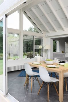 a dining room table with white chairs and plates on top of it in front of large windows