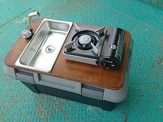 a small stove sitting on top of a wooden table next to a metal pan with a burner