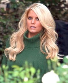 a woman with long blonde hair wearing a green turtle neck sweater