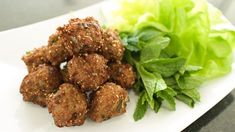 meatballs and lettuce on a white plate next to a green leafy salad