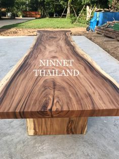 a large wooden table sitting on top of a cement floor in front of some trees