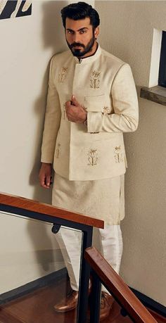 a man in a white outfit standing next to a stair case and looking at the camera