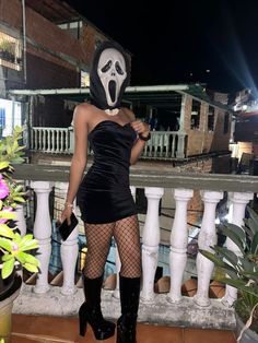 a woman in a black dress and mask standing on a balcony with her legs crossed