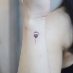 a woman's wrist tattoo with a glass of wine on the left side of her arm