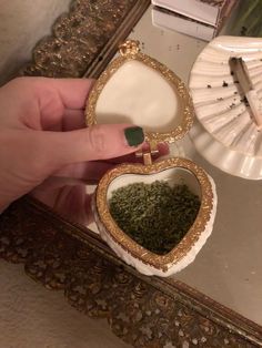 a person holding a small heart shaped box filled with green stuff in front of a mirror