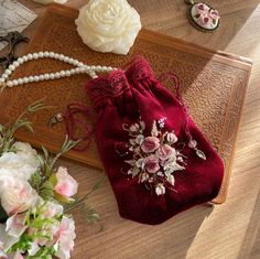 a red velvet bag with flowers and pearls on the table next to other jewelry items