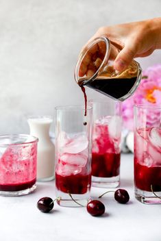 someone pouring red liquid into glasses filled with ice and cherries