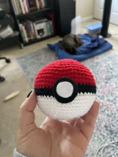 someone is holding up a crocheted pokeball in front of a cat on the floor